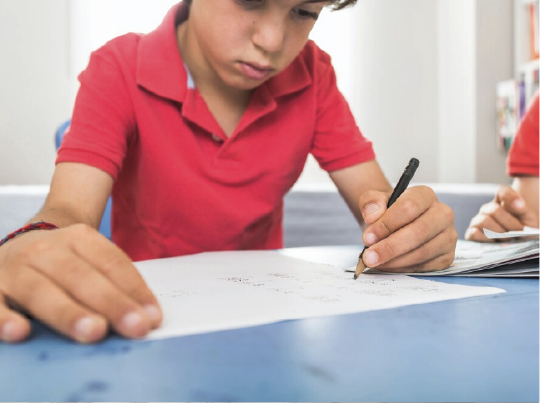 Close up of a boy wearing a red shirt writing on a piece of paper